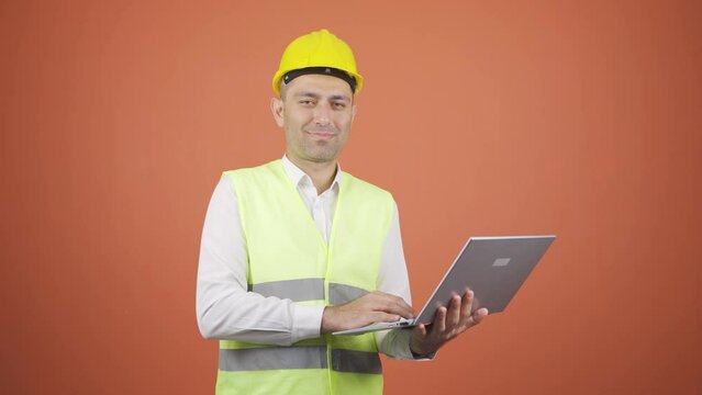 Engineer holding laptop laughing at camera.