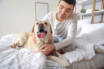 Young man with cute Labrador dog and toy sitting in bedroom