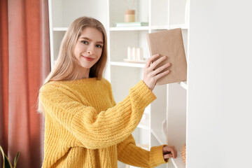 Young woman taking book from shelf at home