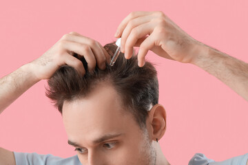 Young man using serum for hair growth on pink background, closeup