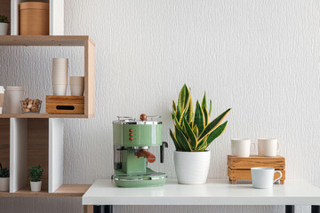 Modern coffee machine, houseplant and takeaway cups on table near white wall