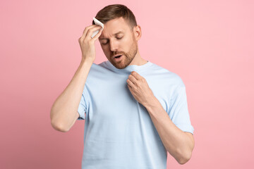 Overheated sweaty man suffering from heat stroke from high weather temperature using paper napkin...