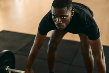 Fototapeta na wymiar Black sportsman lifting barbell at gym