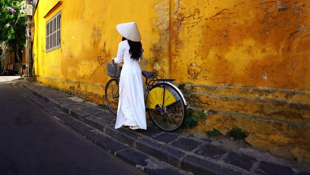 Asian woman wearing vietnam culture traditional and rolls a bicycle at Hoi an, Vietnam.