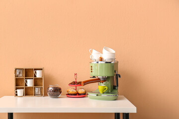 Table with modern coffee machine, cups and snacks near beige wall