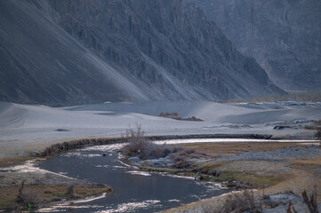 A river stream flows through a white sand desert surrounded by mountain landscapes.