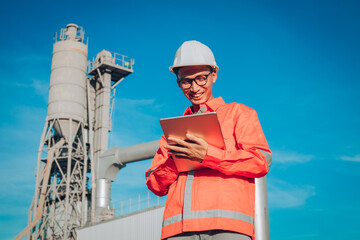 Asian man engineer is standing at plant the production of concrete. Confident asian engineer man Using tablet for checking and maintenance to inspection new project.