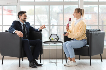 Female journalist with microphone having an interview with man in office