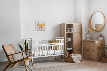 Interior of light bedroom with baby crib, drawers and armchair