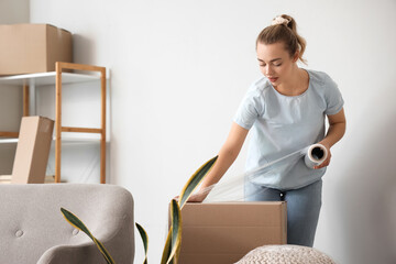 Young woman wrapping cardboard box with stretch film at home