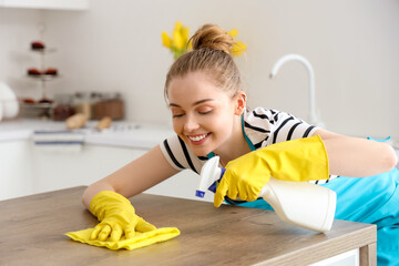 Happy young woman in yellow rubber gloves cleaning dining table with rag and detergent