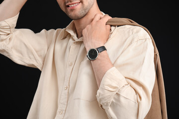 Handsome young man with wristwatch and stylish jacket on black background, closeup