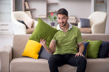 Young man with a lot of pillows sitting on the sofa