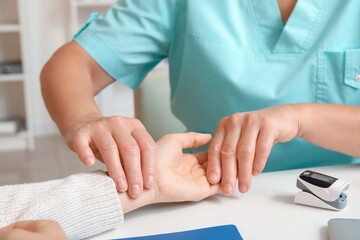 Female doctor checking patient's pulse in clinic, closeup