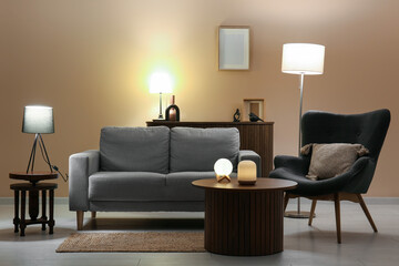 Interior of living room with grey sofa, wooden table, armchair and glowing lamps