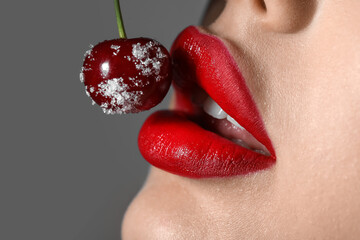 Beautiful woman with red lips and frozen cherry on dark background, closeup