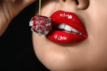 Beautiful woman with red lips and frozen cherry on black background, closeup