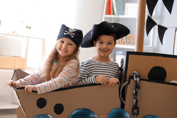 Cute little pirates playing in cardboard ship at home