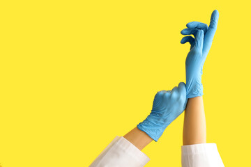 Female doctor putting on medical gloves against yellow background