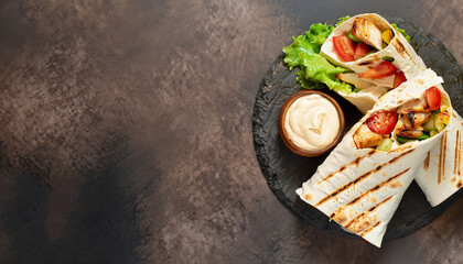 Shawarma pita bread with grilled chicken, fresh vegetables and cream sauce on a background of brown stone. Top view with copy space. - obrazy, fototapety, plakaty