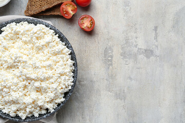 Fresh cottage cheese in bowl with bread pieces and tomatoes on grey table