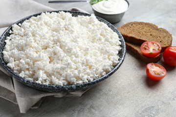 Fresh cottage cheese in bowl with bread pieces and tomatoes on grey table