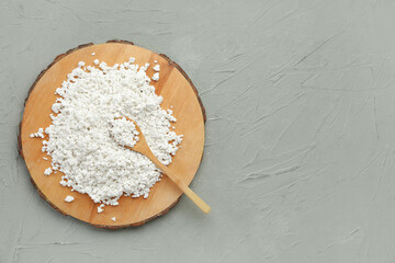 Wooden board with fresh cottage cheese and spoon on grey table