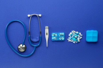Stethoscope, pills and digital thermometer on blue background