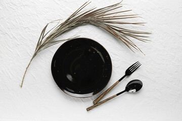 Clean black plate, cutlery and dry branch on white table - obrazy, fototapety, plakaty
