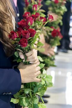 a photography of a woman holding a bunch of red roses, there are many people standing in line holding red roses.