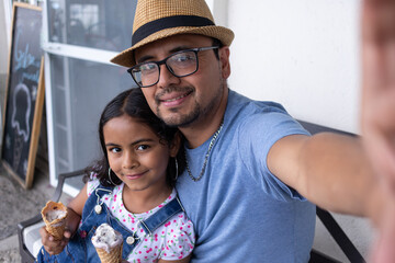 selfie of a hispanic young father eating gelato ice cream with his child girl, selfie of dad and...