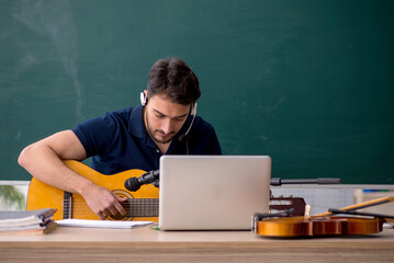 Young male music teacher sitting in the classroom