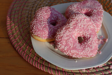 Pink glazed donuts in shape of a heart on a white plate on wooden table