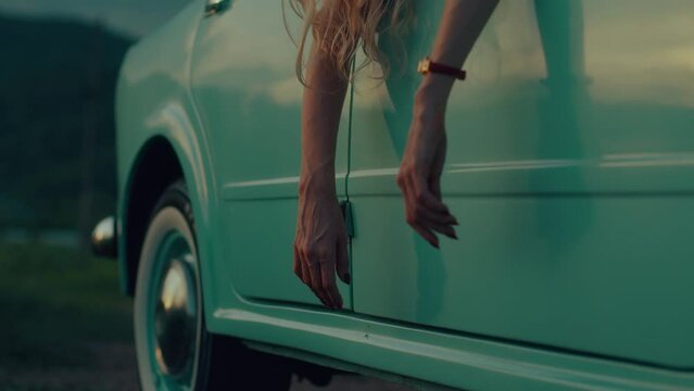 female hands dangle from the door of a retro car