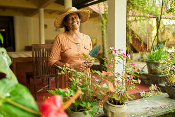 Senior Indian female farmer in straw hat with gardening scoop in garden. Elderly Sri Lankan happy...