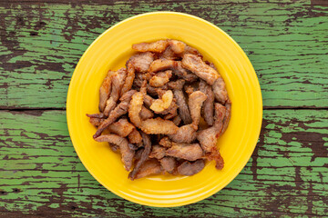 tasty fried pork in yellow ceramic plate on rustic old green natural wood texture background, top view, flat lay, street food
