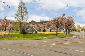an intersection in the middle of a city with trees and flowers on both sides, some cars are driving...