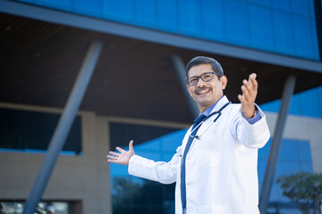 Confident Indian doctor spreading hand and giving happy expression out of hospital.