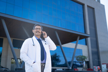 medical concept. Indian doctor standing out of hospital and talking on mobilephone.