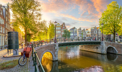 Soul of Amsterdam. Early morning in Amsterdam. Ancient houses, bridges, traditional bicycles, canals and the sun shines through the trees. View of all the sights of Amsterdam.