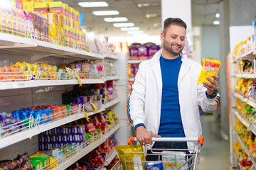 Young indian man looking product detail and purchasing at grocery shop.