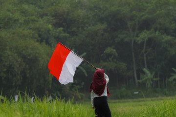 Asian woman in white shirt waving Indonesian flag excitedly in rice field