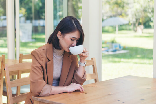 Beauty woman drinking black coffee in coffee shop holding freshness cup. Coffee lover. Asian Woman drink black coffee hand holding cup at green garden cafe. Young woman smile face love drink coffee