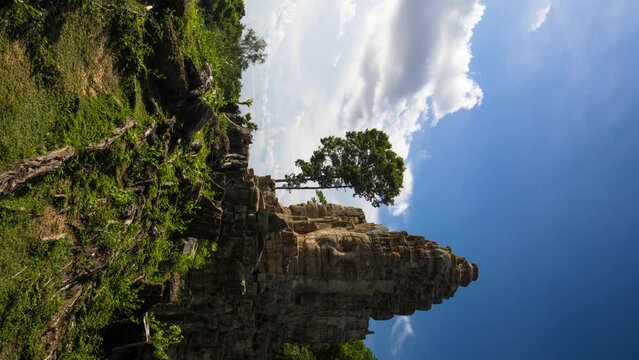 Angkor temple.  West gate of Angkor Thom.  Giant buddhist faces overlook the entrance to Angkorian city.  Timelapse vivid blue polarised sky and fluffy white clouda, vertical footage copy space.