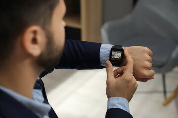 Businessman checking home security system via smartwatch app in office, closeup. Image of room...