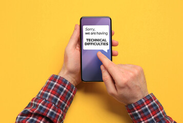Man received message Sorry We Are Having Technical Difficulties on smartphone on yellow background,...