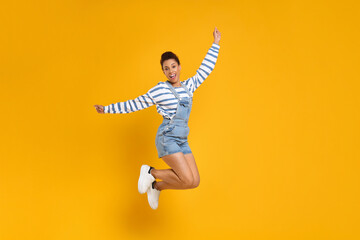 Fototapeta na wymiar Happy young woman jumping while dancing on orange background