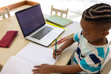 African american boy at desk in online class drawing and using laptop with copy space
