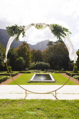 Decorative wedding arch and pond in sunny garden, copy space