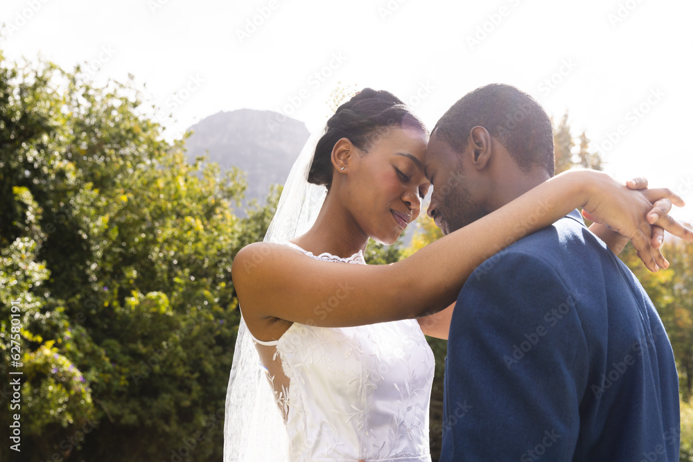 Wall mural Happy african american bride and groom embracing at wedding in sunny garden